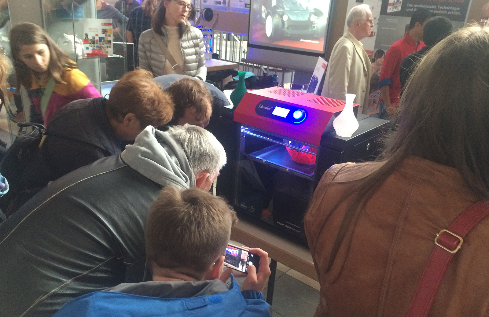 Besucher betrachten den 3D-Drucker beim Druckvorgang.